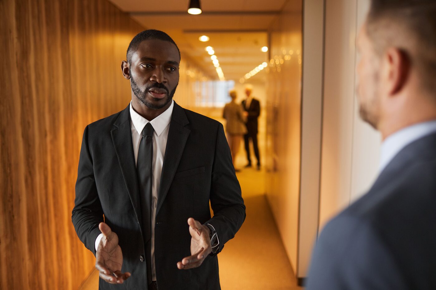 Two professionals in business attire talking in an office hallway