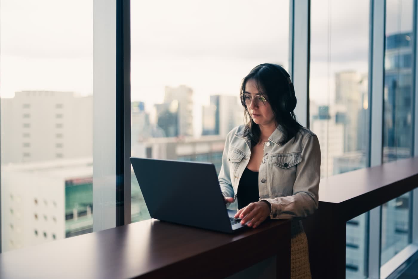 A person working on a laptop at a window counter in a modern office building